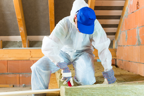 Worker in overall is cutting insulating material with gloves and knife